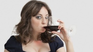 Portrait of beautiful young woman drinking wine against gray background